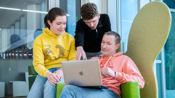 3 masterstudenten zitten samen met een laptop op schoot