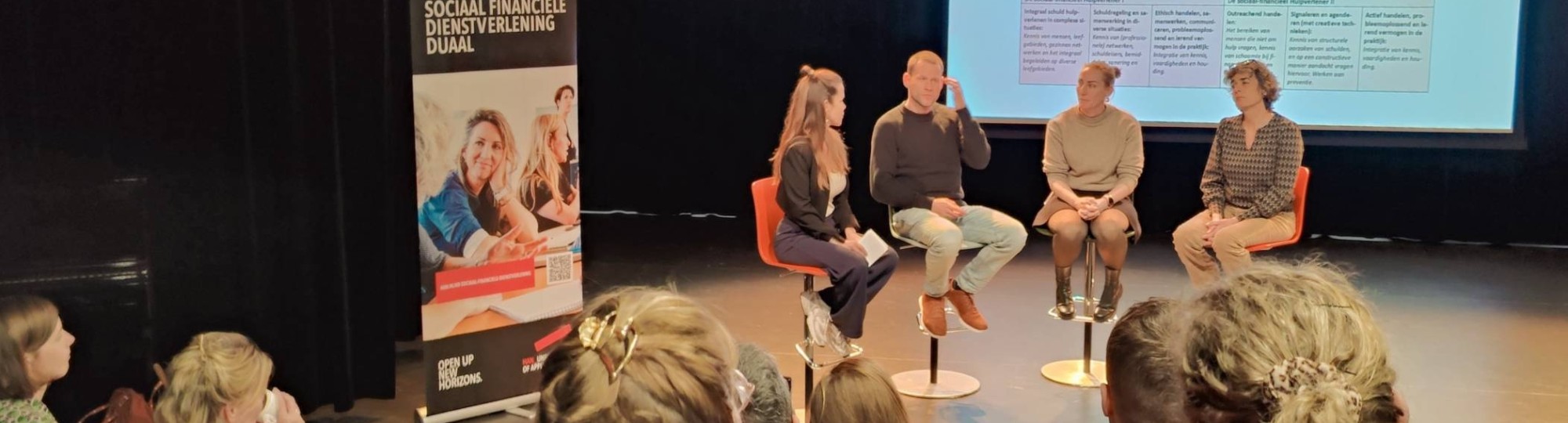 sfeerbeeld van dialoogsessie werkveldpartners sociaal financiële dienstverlening met op het podium docenten en student Daan