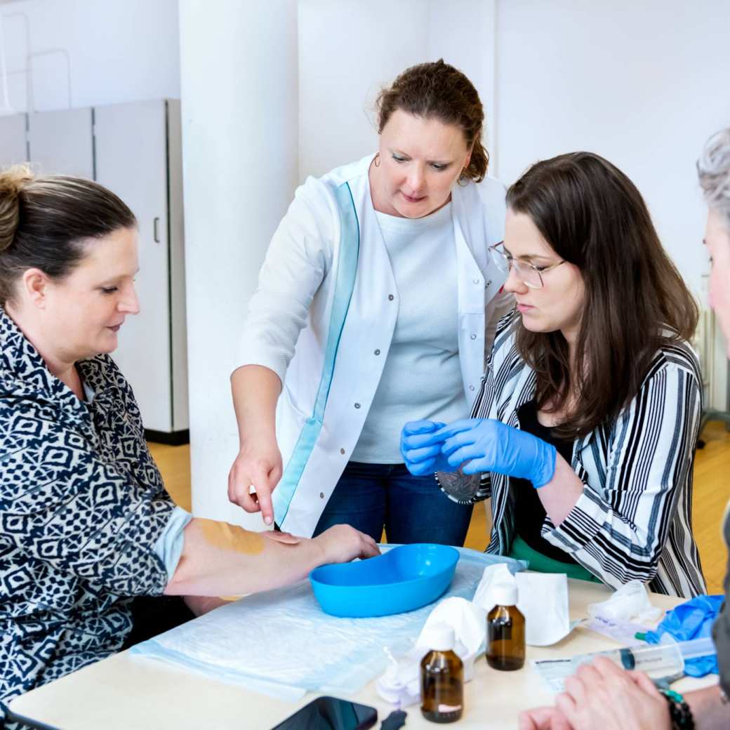 Docent geeft aan 3 studenten uitleg over wondverzorging tijdens les Verpleegkunde deeltijd