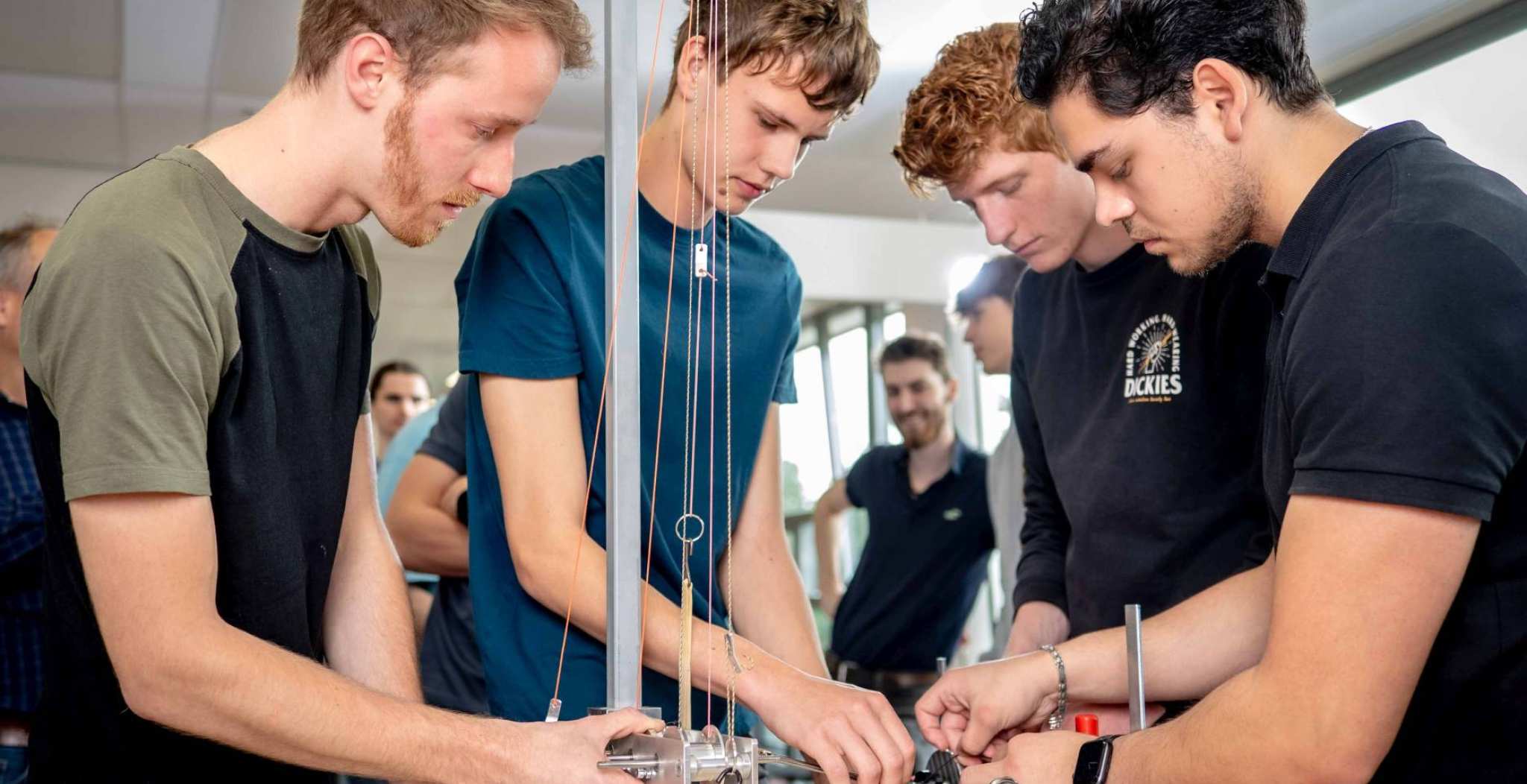 Vier studenten werktuigbouwkunde doen tests met een katrol en gewichten.