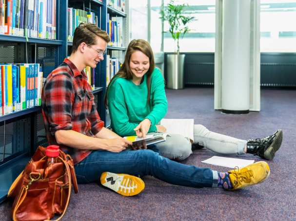 jongen en meisje studeren samen op de grond in studiecentrum en zij wijst iets aan