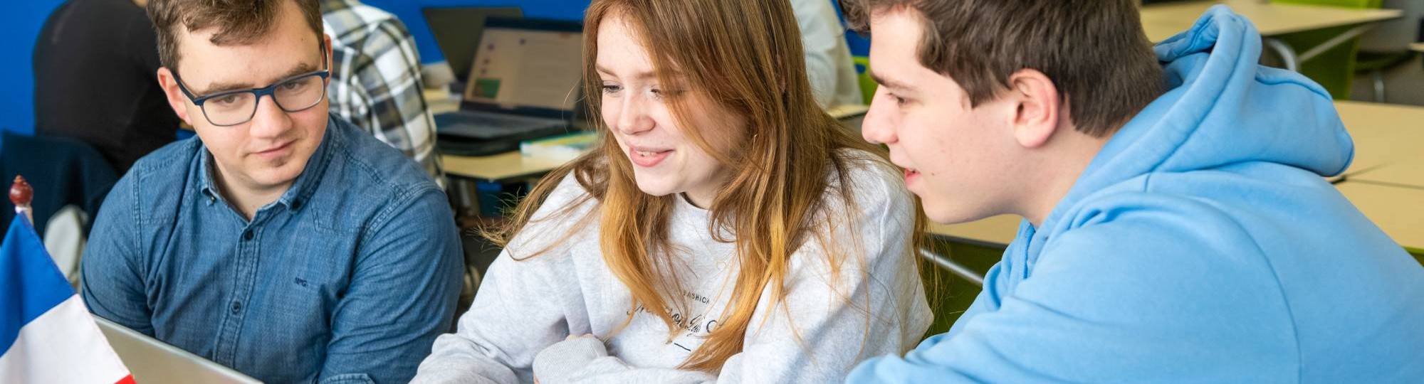 Drie studenten Leraar Frans krijgen uitleg van hun docent die tussen hen in staat.