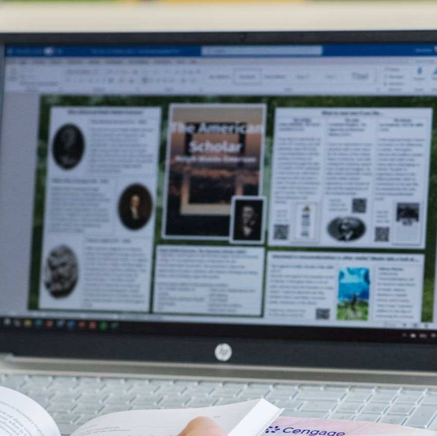 Foto Master Academie Educatie. Een masterstudent zit achter haar laptop met een boek opengeslagen in haar handen. 