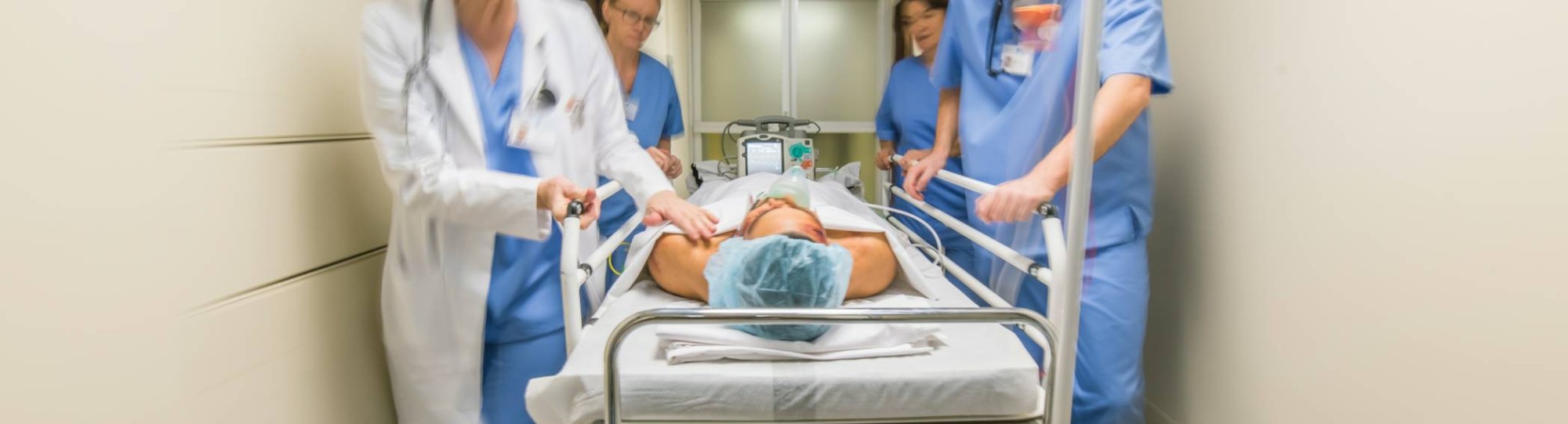 Medewerkers van de spoedeisende zorg lopen met spoed met een patiënt in bed door de gang van een ziekenhuis.