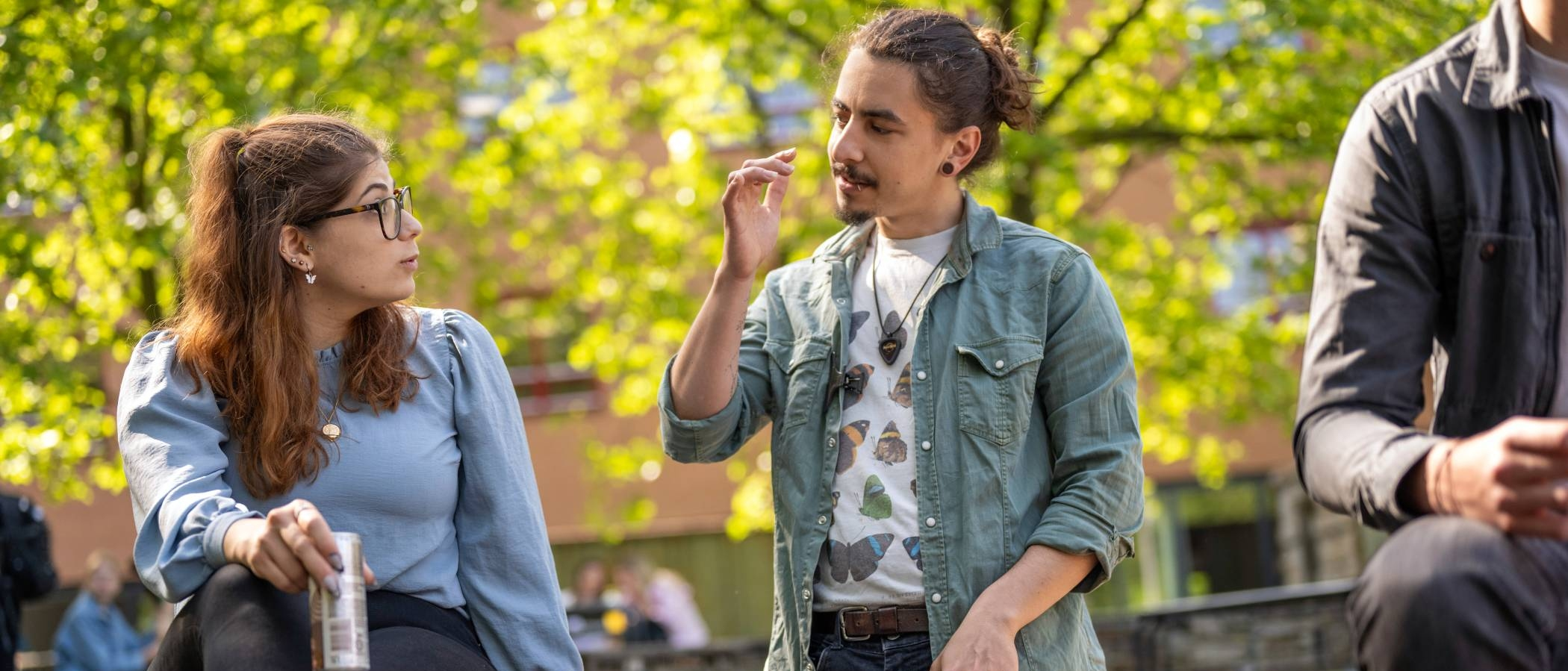 Twee studenten, jongen en meisje, zitten buiten bij K33 en kletsen met elkaar. 