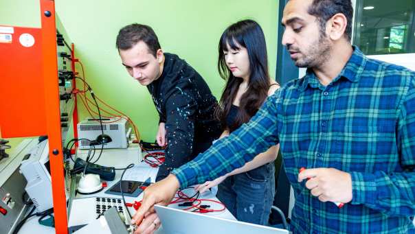 Een elektrotechniekdocent geeft uitleg over een zonnepaneel aan studenten.