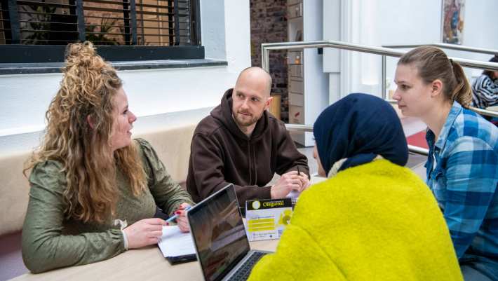 Een groep van 4 studenten overleggen aan zittend een tafel.