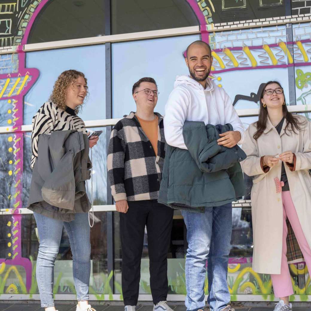 Groep student en een docent lachend voor een vrolijke wand