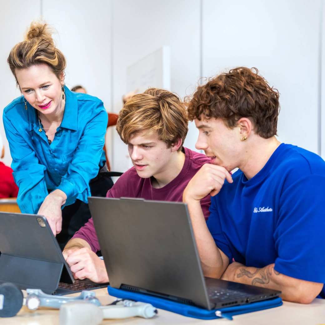 Docent legt iets uit aan twee voltijd studenten.