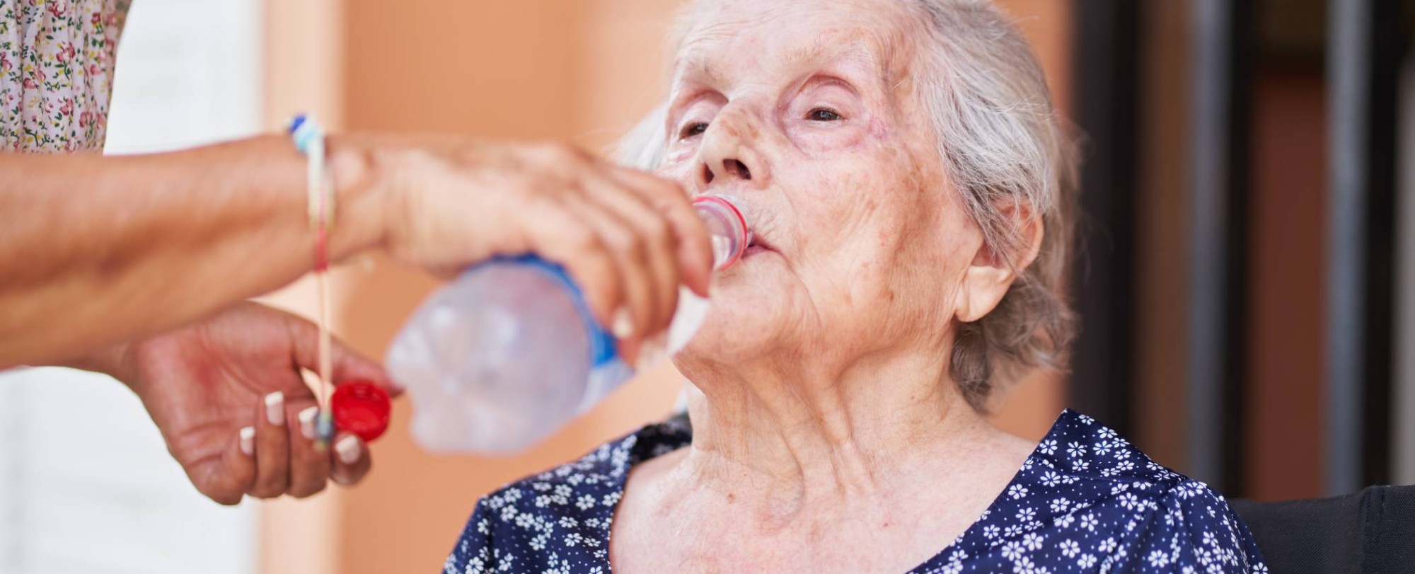 Een oude vrouw drinkt uit een flesje.