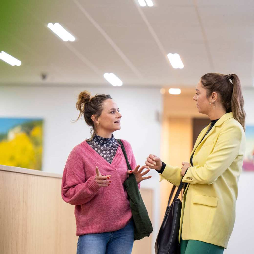 2 studenten lopen overleggend in de gang.