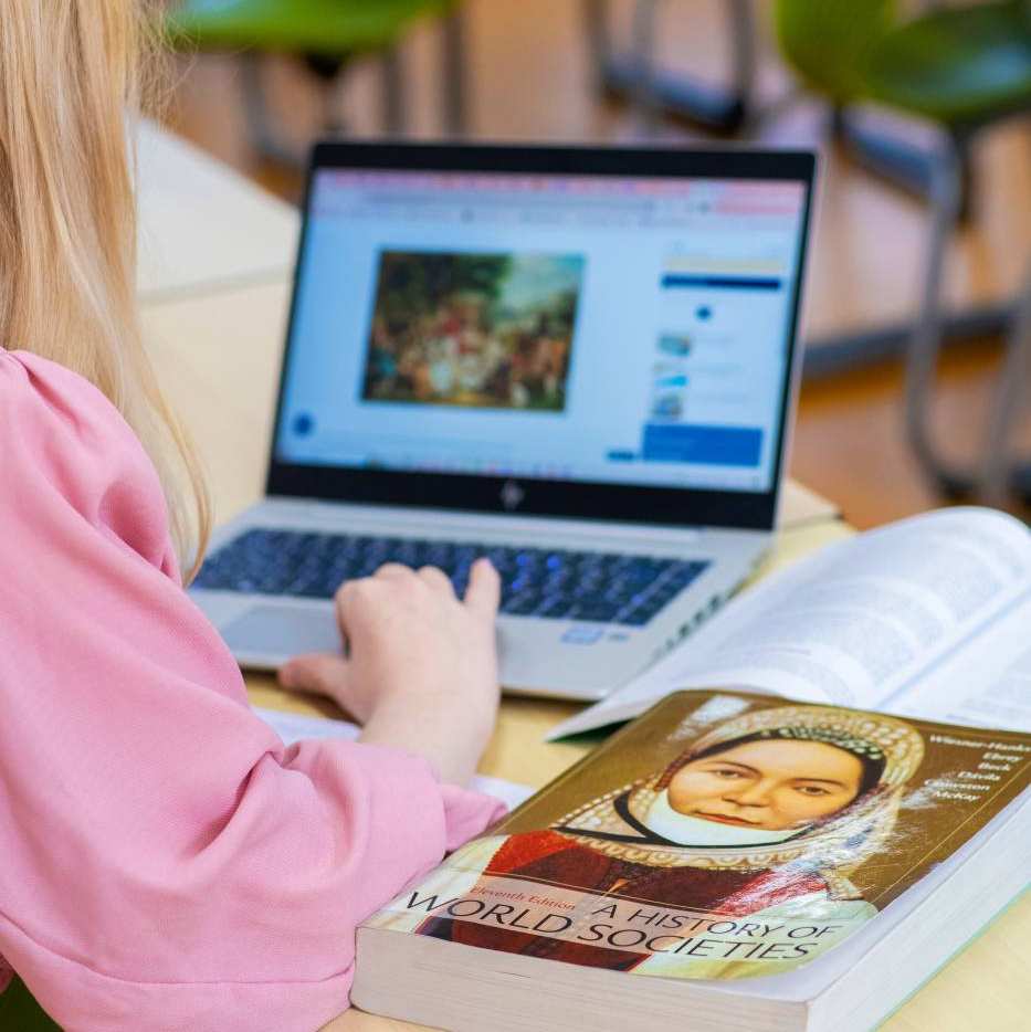 De student wijst iets aan op een poster, terwijl de docent en twee studenten toekijken.