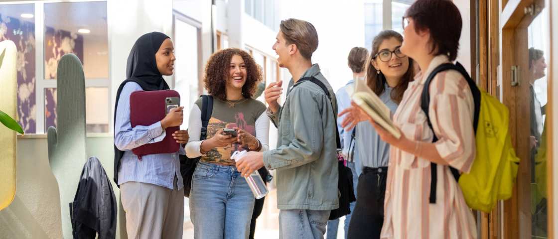 Een groepje studenten staan te wachten voor de klas en hebben plezier. 