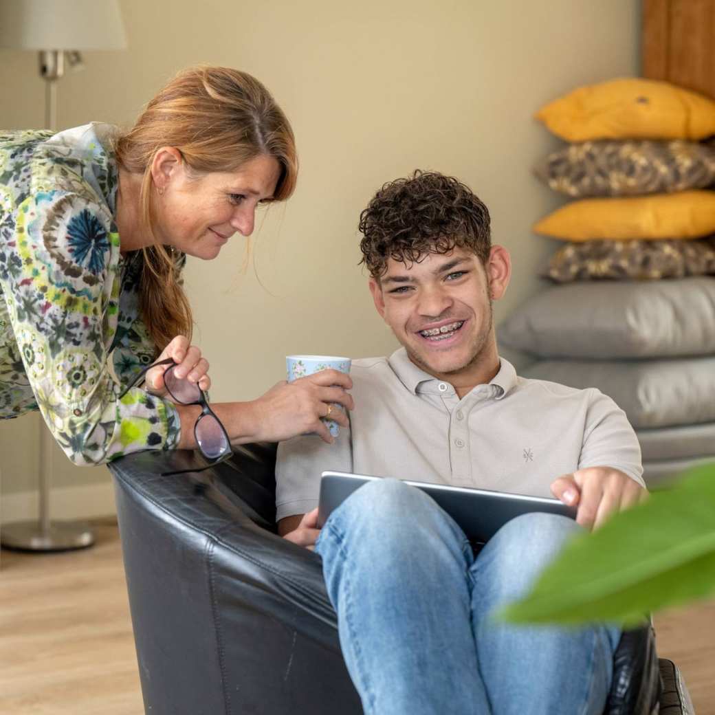 Moeder en zoon lachen terwijl ze hangen in een stoel en bezig zijn op de laptop. 