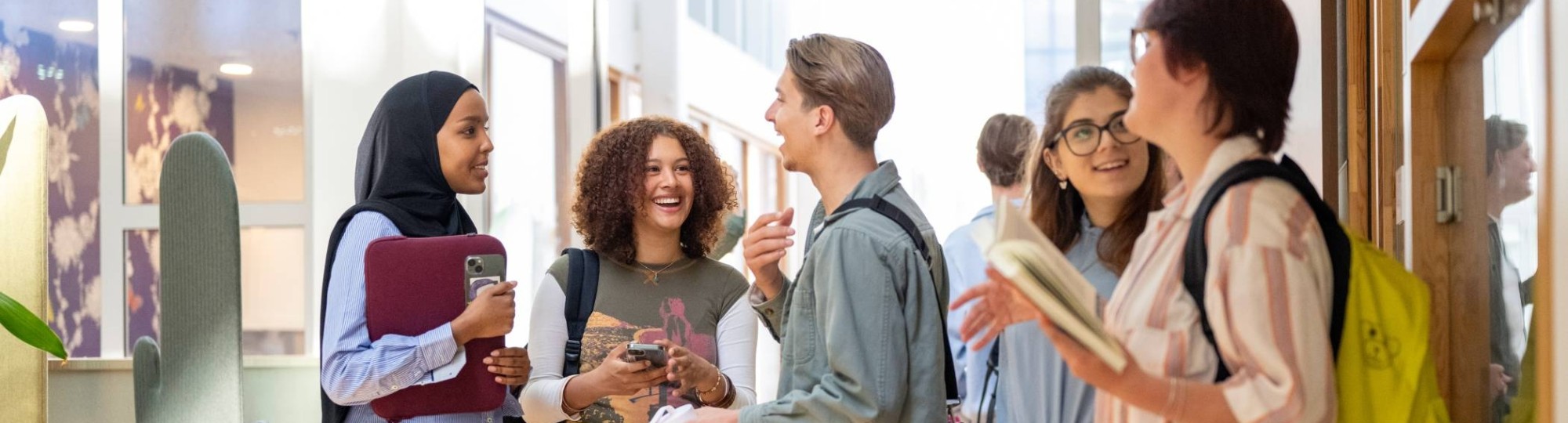 Een groepje studenten staan te wachten voor de klas en hebben plezier. 