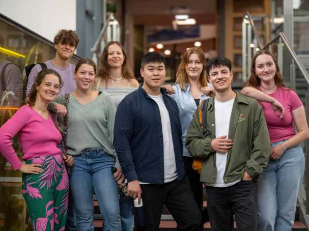 Groep studenten lachen in de camera, staan in de lichtstraat van gebouw R26. 