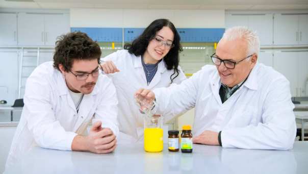 Twee studenten zijn met docent in het lab een proef aan het uitvoeren.
