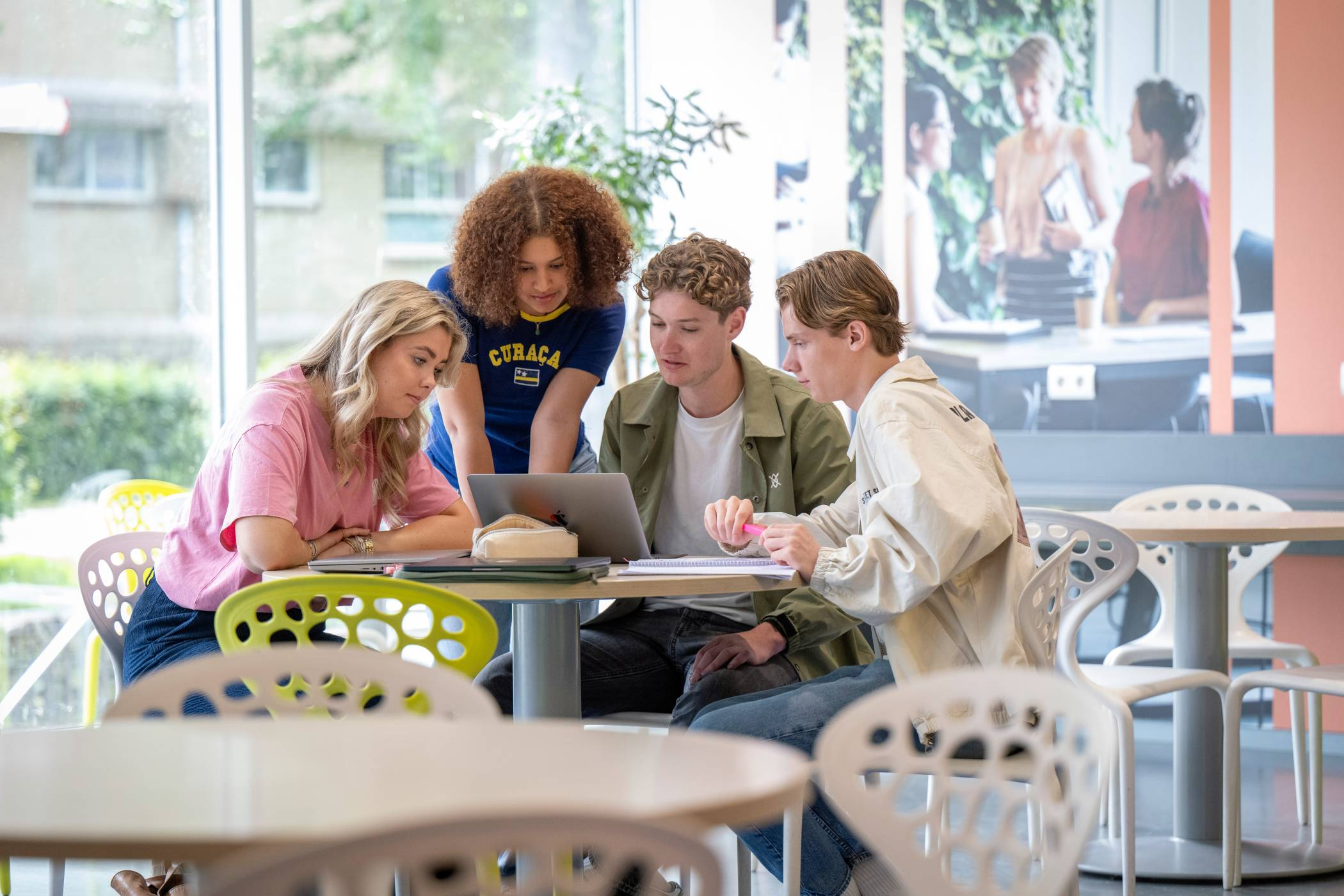 Groepje studenten werken samen aan een ronde tafel in de gang, werkplek in LvS10. Kijken samen naar de laptop.