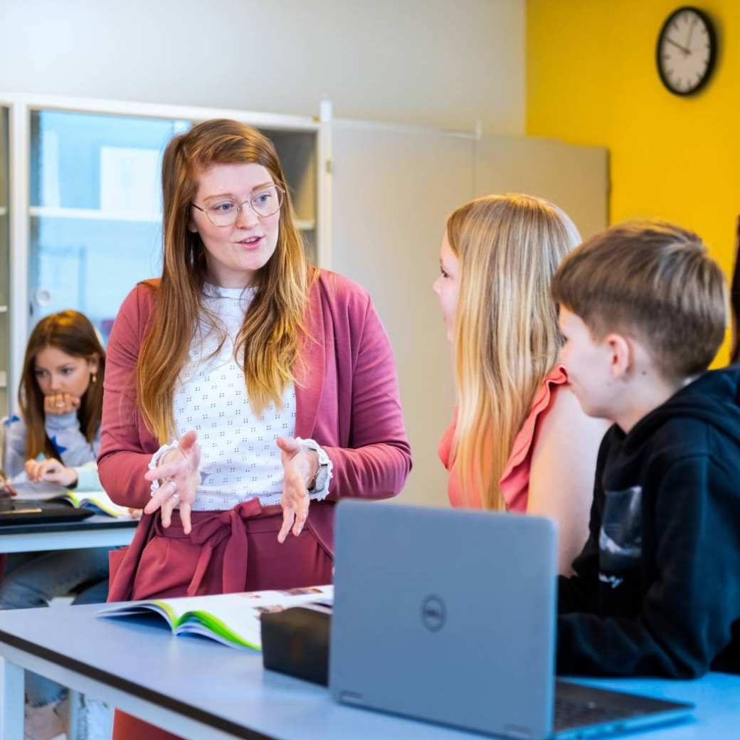 De docent geeft uitleg aan twee scholieren met handgebaren