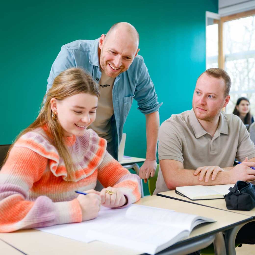 De docent kijkt mee over de schouder van de studenten.