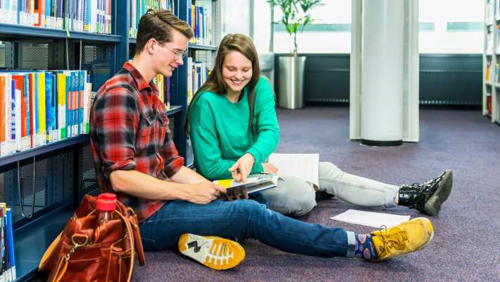 jongen en meisje studeren samen op de grond in studiecentrum en zij wijst iets aan