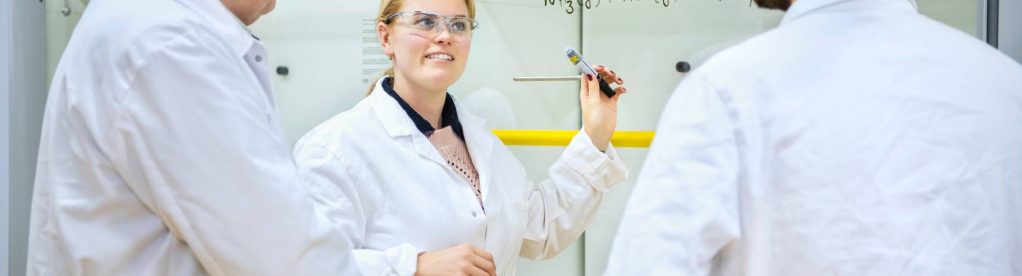 Twee studenten Leraar Scheikunde voeren een experiment uit en hebben een labjas aan en een veiligheidsbril op.