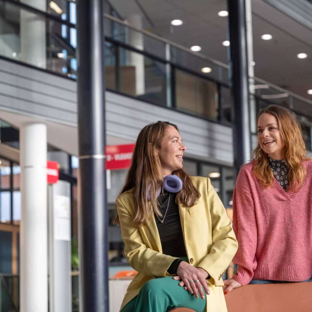 2 studenten staan en zitten in een hal.