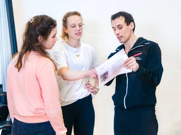 Docent helpt studenten en legt wat uit met behulp van een blaadje. 