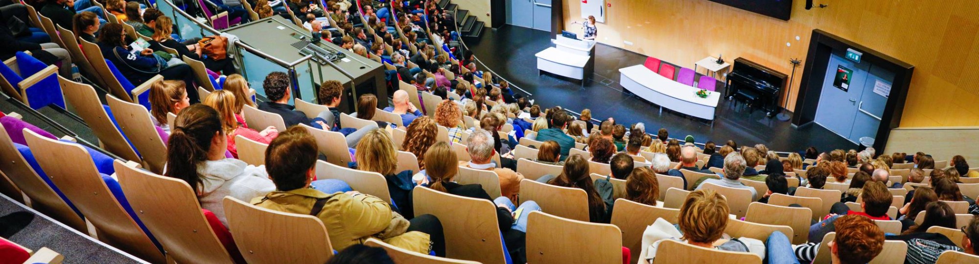 Beeld van bovenaf in auditorium met volle zaal voor presentatie houten look