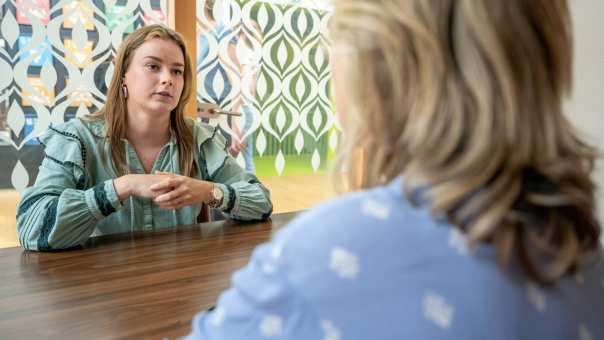 Student is in gesprek met een docent, zitten samen in een hokje. Studentbegeleiding. 