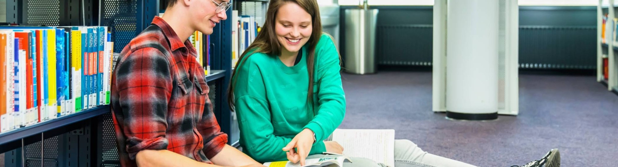 jongen en meisje studeren samen op de grond in studiecentrum en zij wijst iets aan