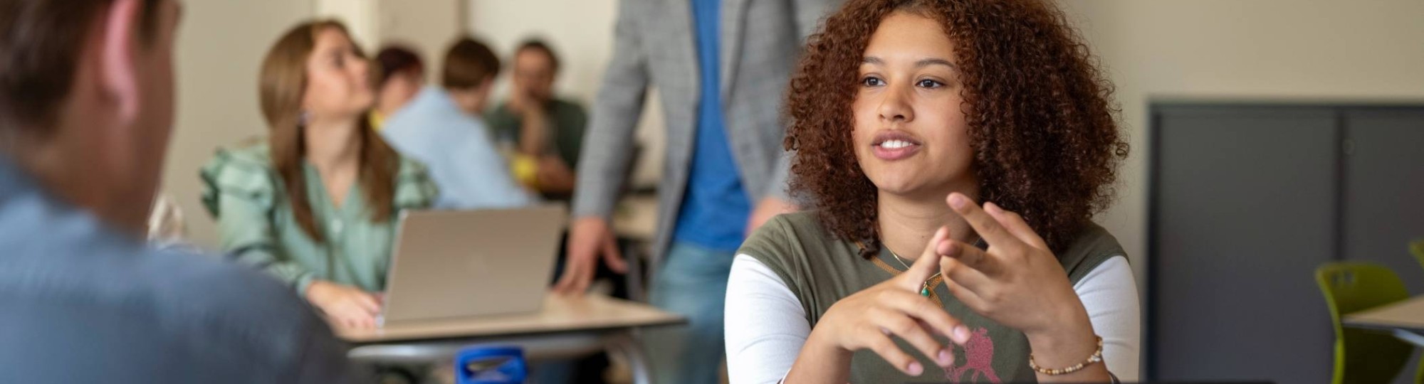 Meisje student in gesprek met jongen, in de klas, met laptop.