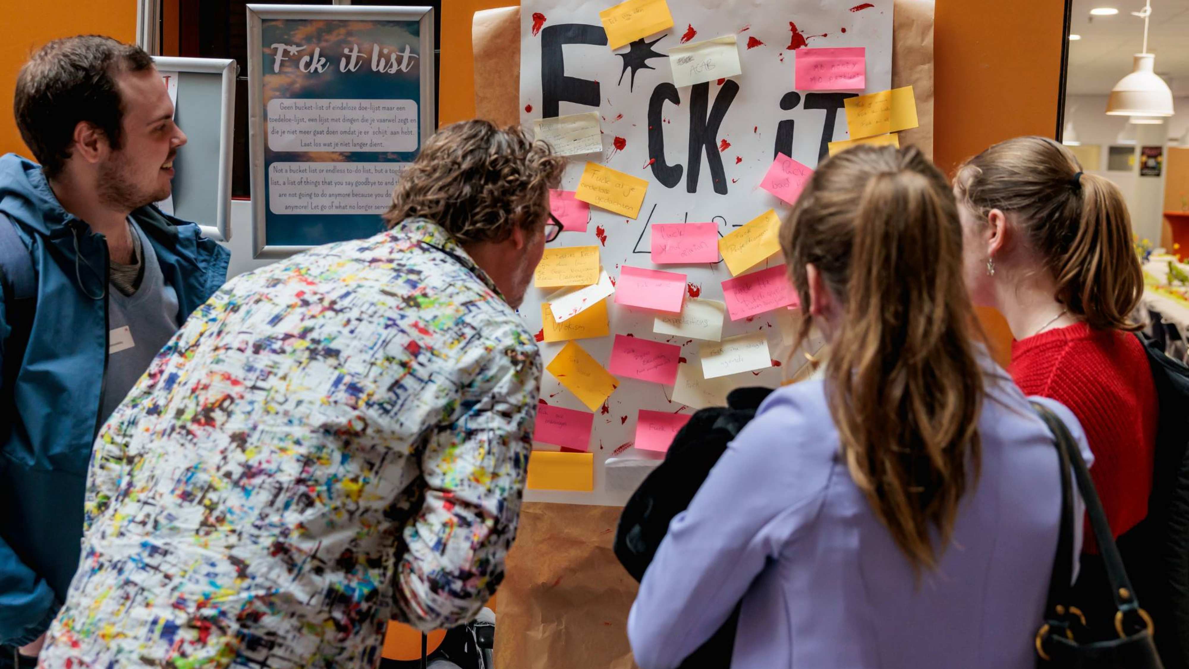Deelnemers van festival LOS bekijken welke boodschappen zijn geschreven op de poster op een oranje muur