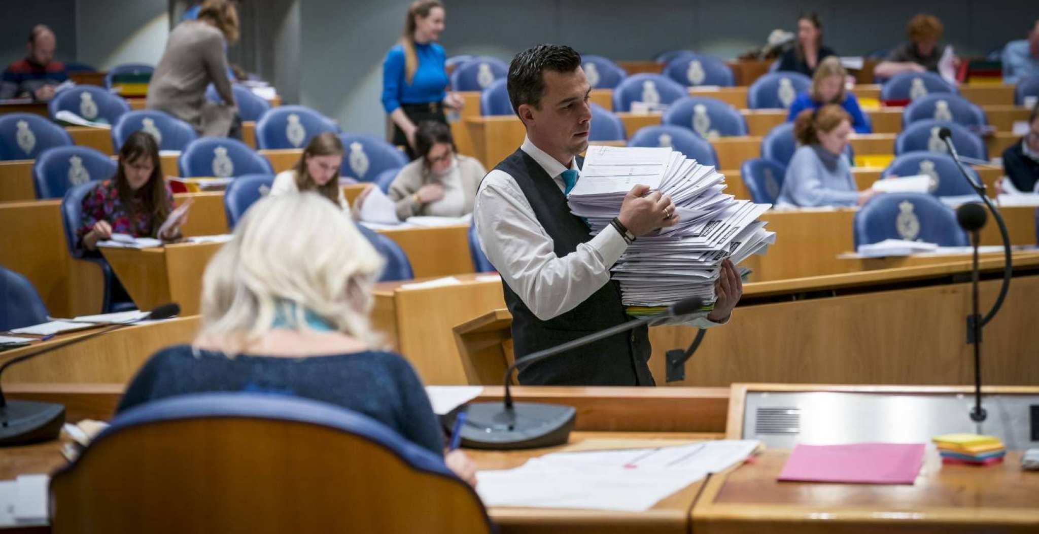 Een medewerker van de Tweede Kamer verzamelt documenten in de Plenaire Zaal.