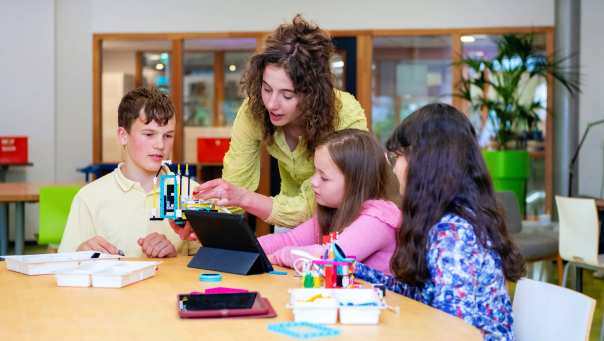 Een student heeft speelgoed vast, terwijl de kinderen toekijken. 