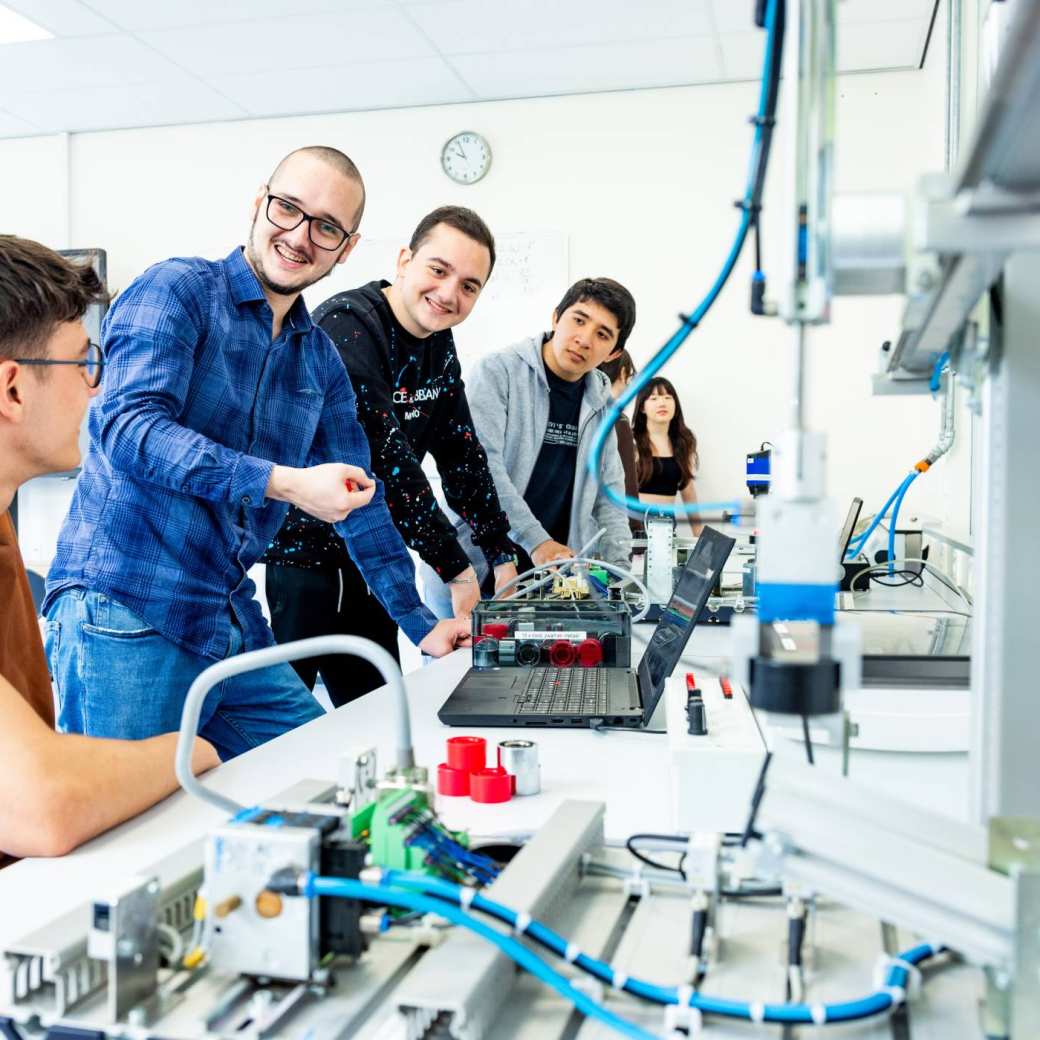 Docent en studenten elektrotechniek  aan een Programmable Logic Controller (PLC).