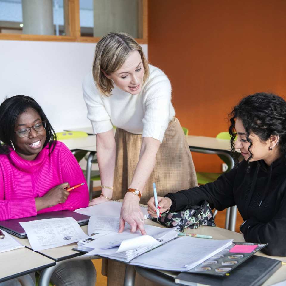 docent van de Educatie masteropleidingen geeft uitleg aan tafel bij 2 studenten