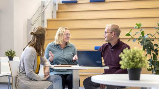 3 studenten in gesprek aan tafel met een laptop.