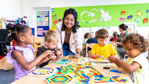 Kinderen leggen een puzzel in de klas en de lerares van de opleiding leraar basisonderwijs helpt hen hierbij