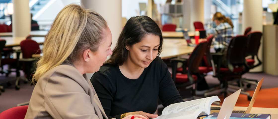 Twee studenten aan het werk in de bibliotheek en kijken naar een boek voor studie PMT deeltijd