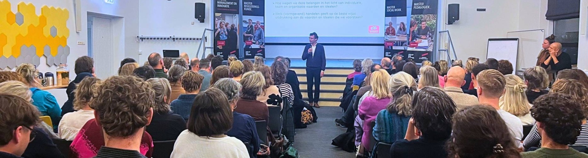 beeld van aula aan de groenewoudseweg waar deelnemers aan het kennisevent wijs leiderschap op stoelen zitten in de zaal