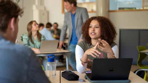 Meisje student in gesprek met jongen, in de klas, met laptop.