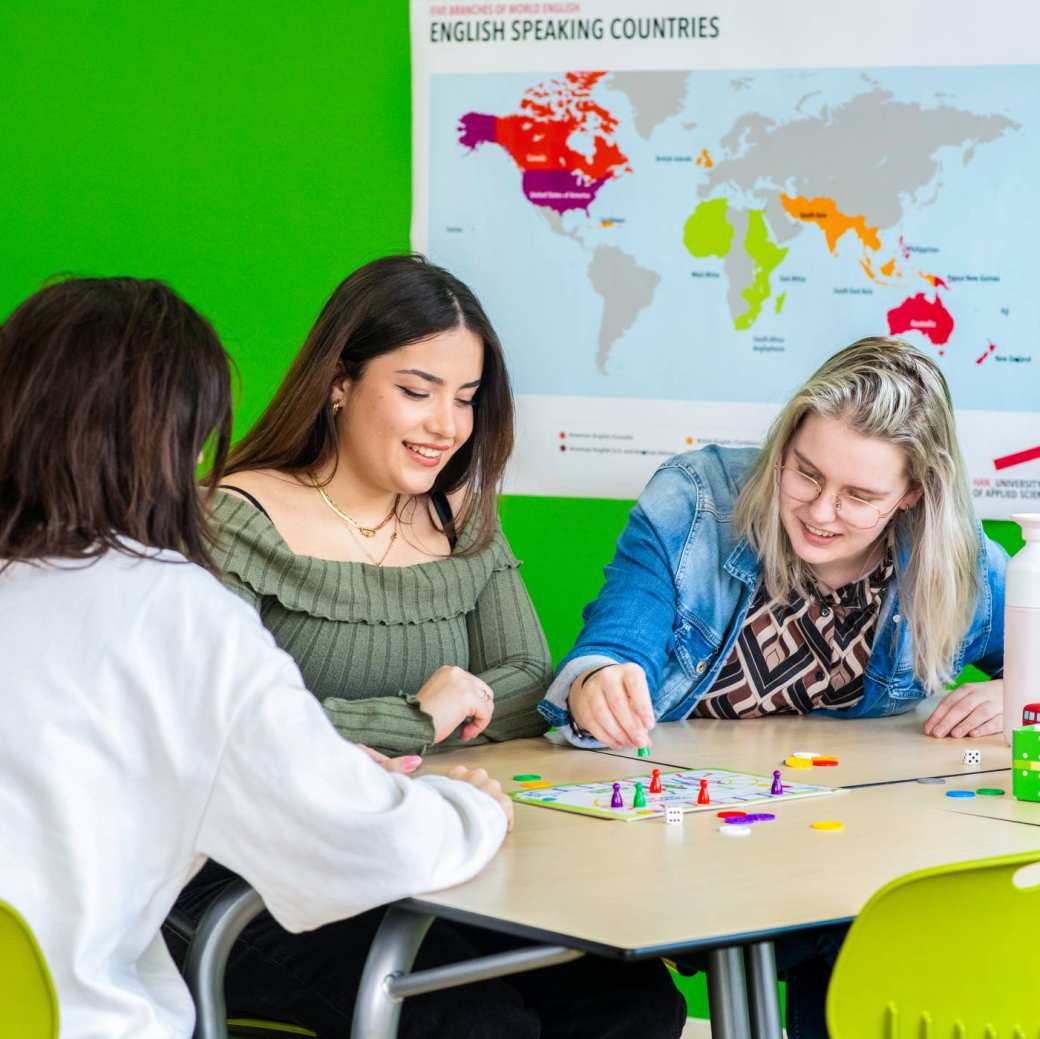 Drie studenten spelen in een lokaal waar de Engelse vlag hangt 'Mens, erger je niet!'
