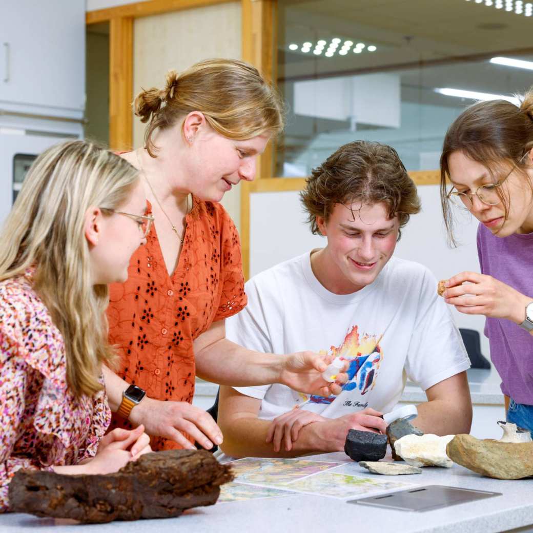 Eén docent en drie studenten onderzoeken samen stenen in het lab.