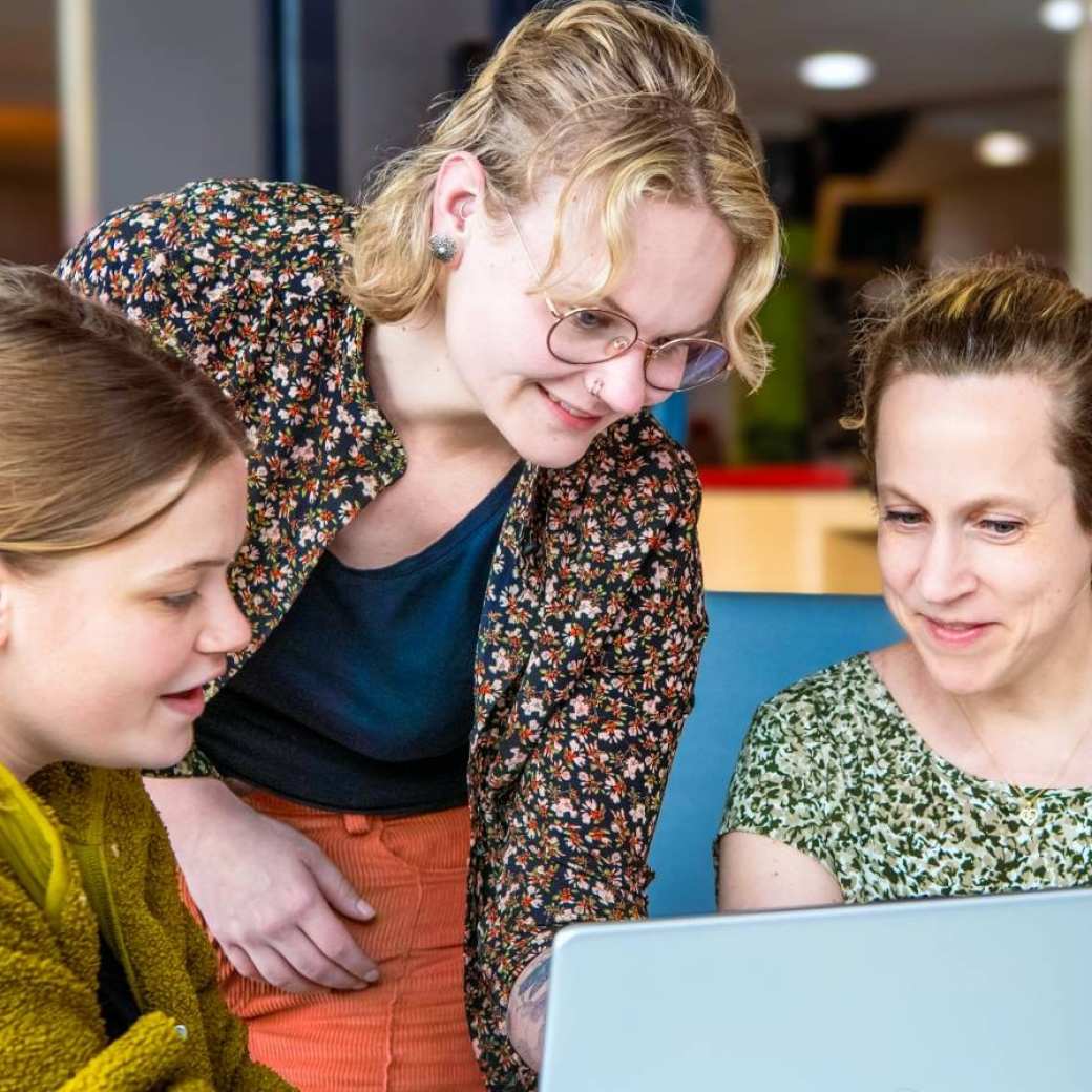 3 studenten kijken samen naar de laptop en overleggen met elkaar