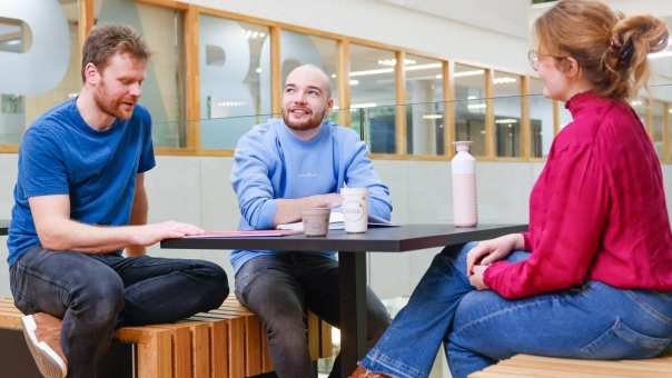 Drie studenten zitten en praten op de gang