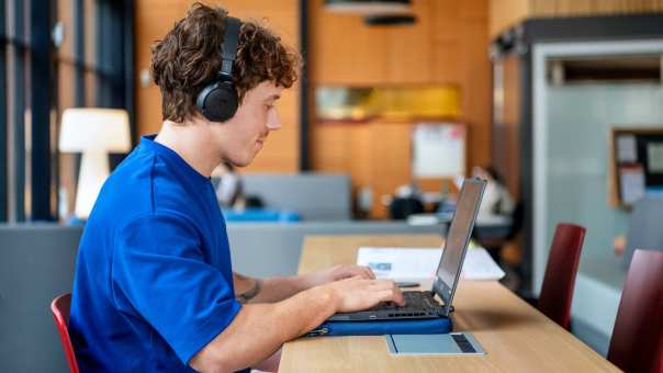 Student met koptelefoon werkt achter computer.