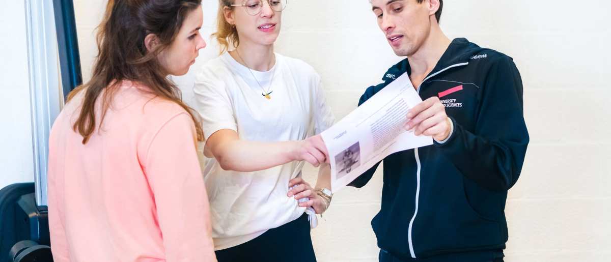 Docent helpt studenten en legt wat uit met behulp van een blaadje.