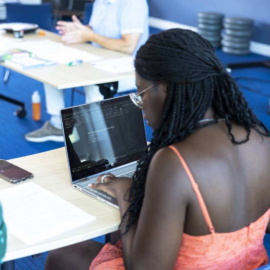 Student van de Master Social Work maakt aantekeningen op laptop terwijl de docent uitleg geeft.