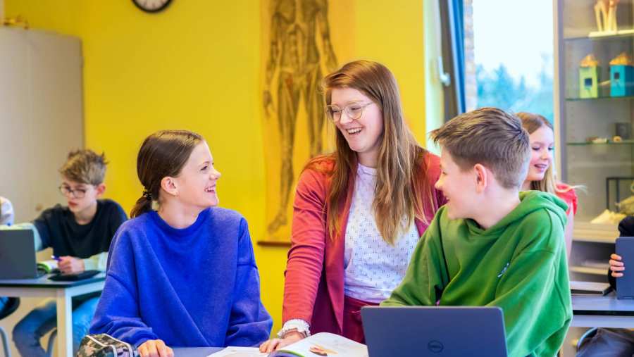 Fotoshoot op het Citadel 2024. De docente lacht met 2 scholieren in de klas. 